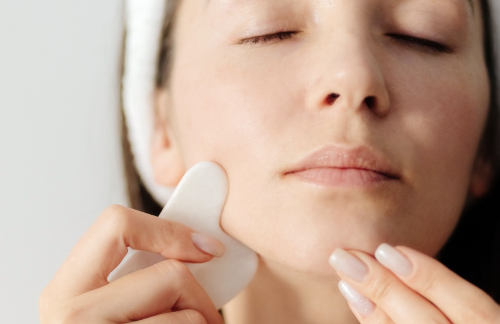 femme qui se fait un face sculpting avec un gua sha blanc